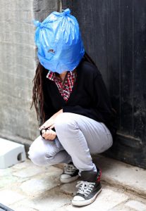 A woman crouching wearing a blue plastic bag over her face.
