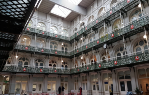 A photograph showing the inside the Hop Exchange, by Lorraine Stoker. This is a view of the central hall, with three levels of balconies around the hall, all decorated with green ironwork with red details, and a huge skylight.