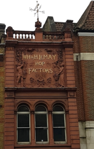 A photograph showing WH and H le May Hop Factors Southwark by Lorraine Stoker. The building is a terracotta colour, and above the windows the name of the hop factors is displayed along with carvings of idealised hop picking scenes.