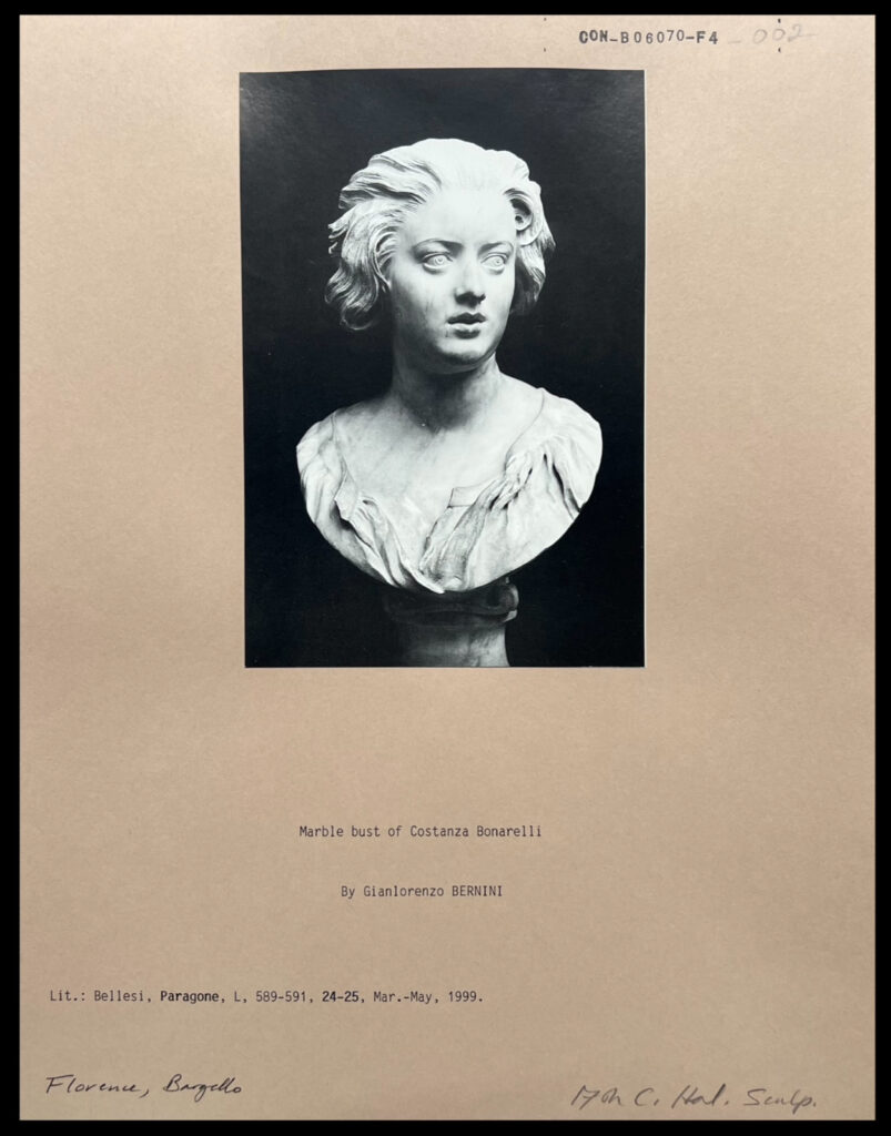 A black and white photograph mounted on card. The photograph depicts a bust of a woman, facing off to her left with her mouth slightly open. She is frowning slightly.