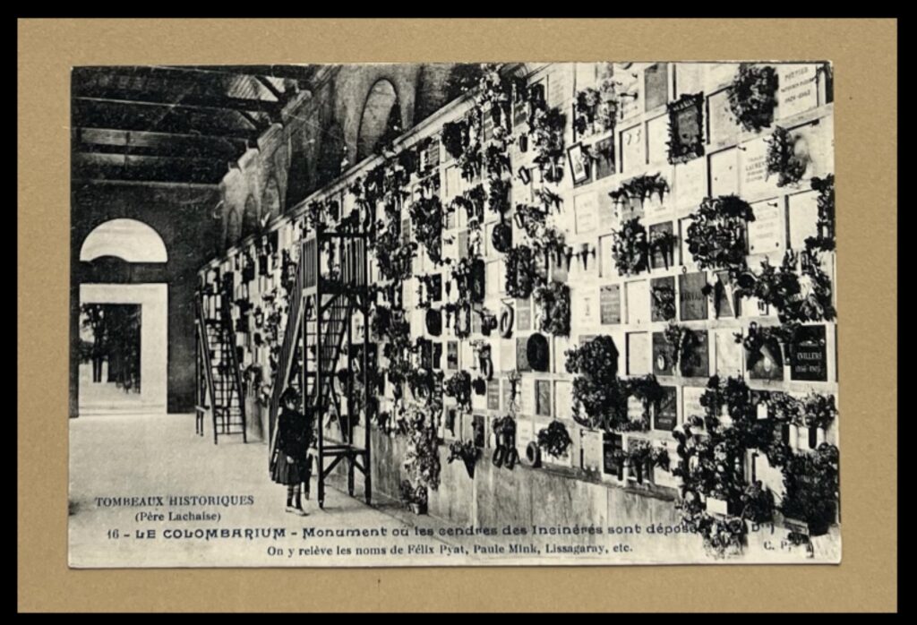 Black and white photograph mounted on card. Depicts a small child standing at the foot of a ladder against a wall that is covered in small memorial plaques and bunches of flowers.