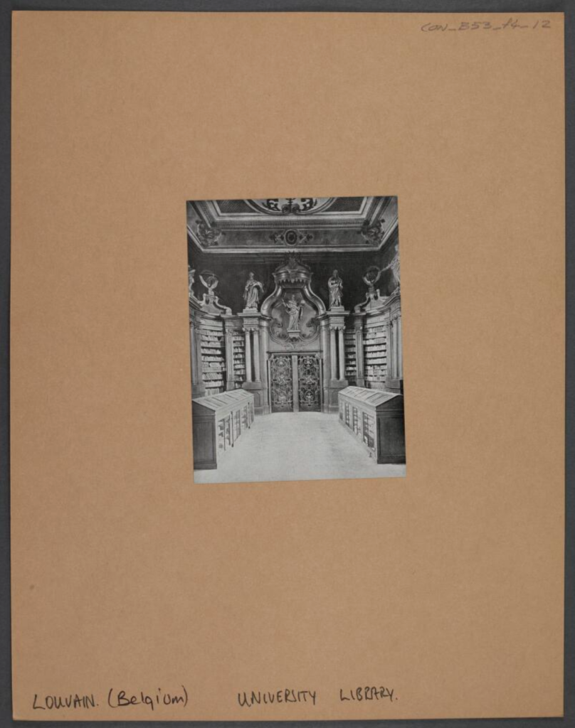 A black-and-white print that shows the interior view of the Université catholique de Louvain library with ornate ceiling, statues and reading stands with glass fronts. Contains wrought iron double door, wall bookshelves, with columns and a crown motif over the main entrance statue.