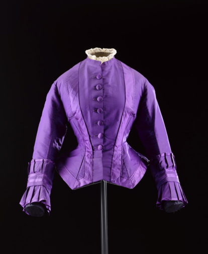 Woman's bodice in purple silk, part of a dress ensemble (A.1977.737.1-3), with high round neckline trimmed with lace, fitted to waist with a flared skirt, fastening centre front with seven buttons, wrist length sleeves, trimmed with purple satin silk: European, possibly British, c. 1870 - 1873 Museum reference A.1977.737.1 Image © National Museums Scotland 