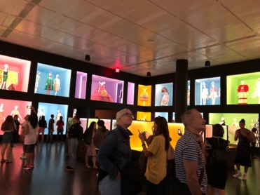 Dark exhibition room with two levels of colorful boxes with mannequins.