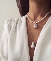 Neck and chest of woman in white shirt with two pearl necklaces of varying size