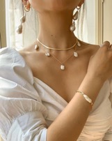 Neck and chest of woman in white shirt with hair up wearing pearl necklace, bracelet, and earrings.