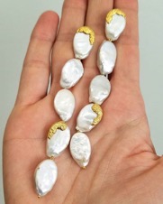 Open palm holding strand of pearl earrings dipped in gold