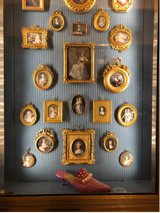 Blue striped wall with gold framed pictures of women and a bright pink decorated show beneath