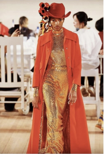 Model in long orange coat and orange hat and gold sequin dress