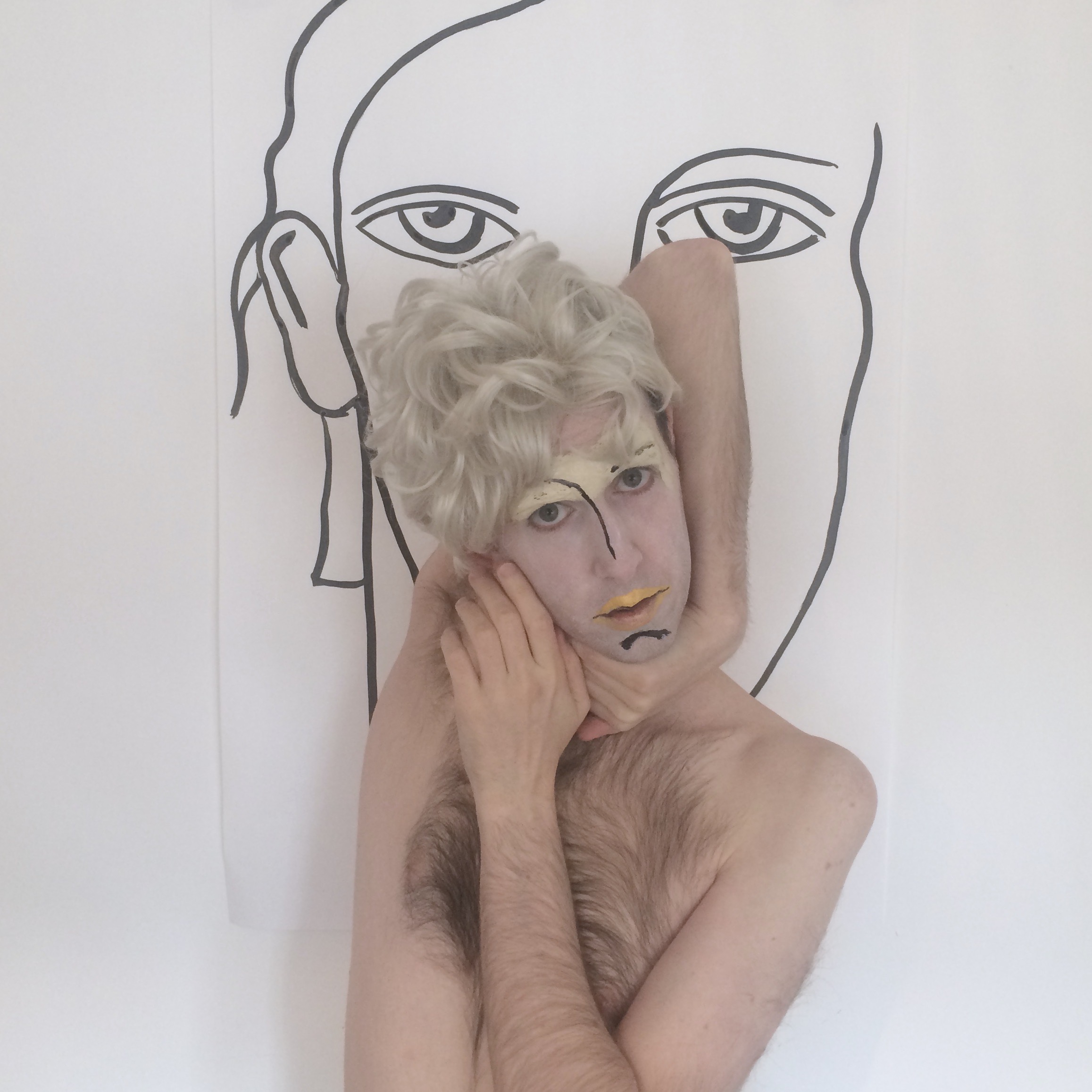 A man in the centre of the image, the top half of his body capture, his arms positioned in a vogue-like pose with his face painted
