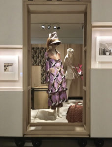 An image taken in an exhibition space, in which a mannequin dressed in elaborate, print ensemble by Louis Vuitton is positioned in the centre of the compostition