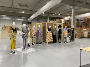 This image was taken in the MOMU store rooms, it is a large and open space with an industrial element to the design, a line of dressed mannequins stand in a line, as though ready to be inspected
