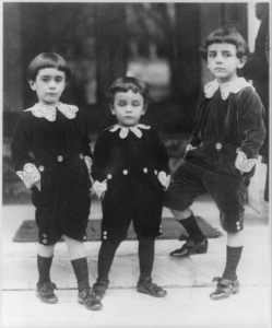 Three young boys posing on a set of steps, all dressed in traditional Lord Fauntleroy suits