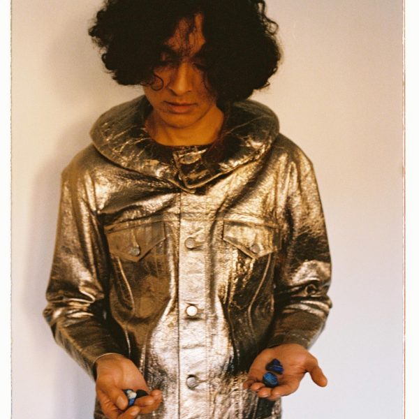 A man, stood centre in front of the camera's lens, dressed in a gold foiled leather "space suit"
