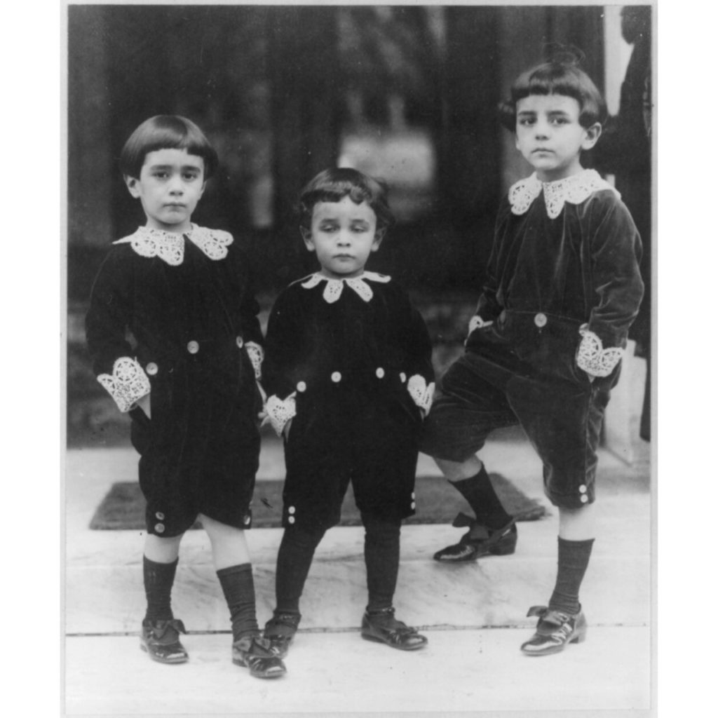 Three young boys posing on a set of steps, all dressed in traditional Lord Fauntleroy suits