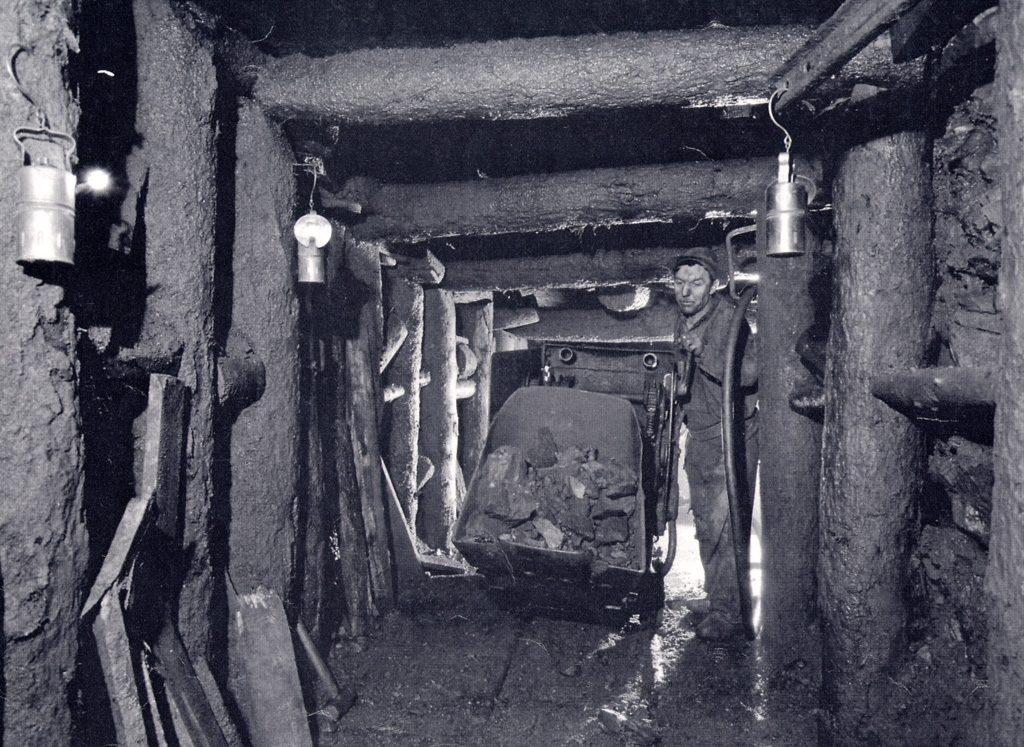 Mine tunnel with miner pushing loaded ore tub