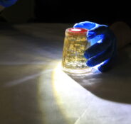 Upside down beaker being lit by a torch with a blue gloved hand holding it