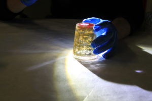 Upside down beaker being lit by a torch with a blue gloved hand holding it