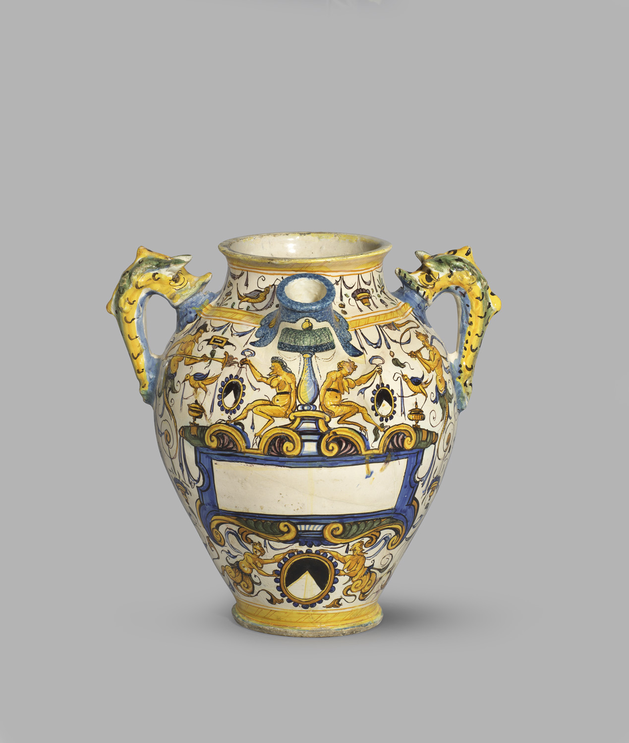 A pharmacy jar with two dragon-shaped handles, painted with fantastical figures in blue and yellow; A space in the centre is left blank to be inscribed with content name or other information