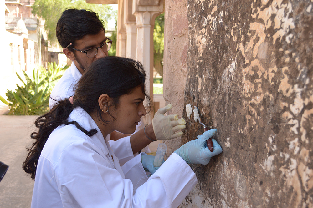 female and male student wearing white lab coats examining a wall painting