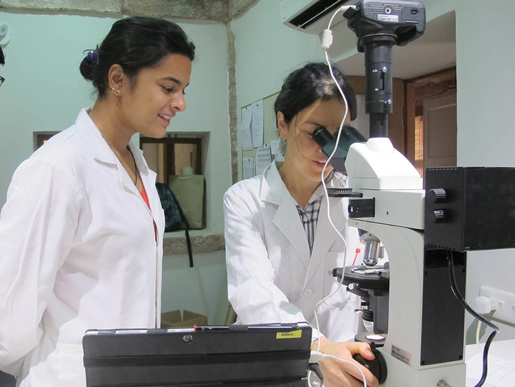two female students wearing a lab coat one is looking at a microscope