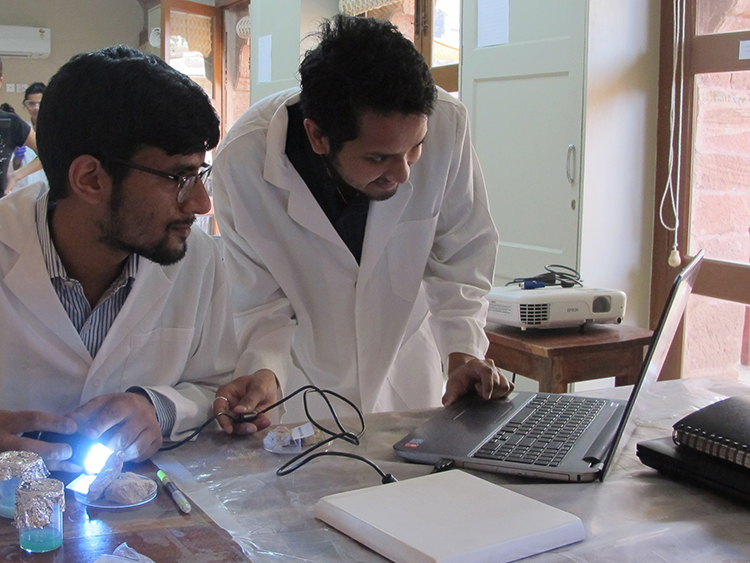 Two male students wearing a lab coat looking at a computer screen
