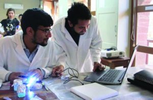 Two male students wearing lab coats looking at a computer screen