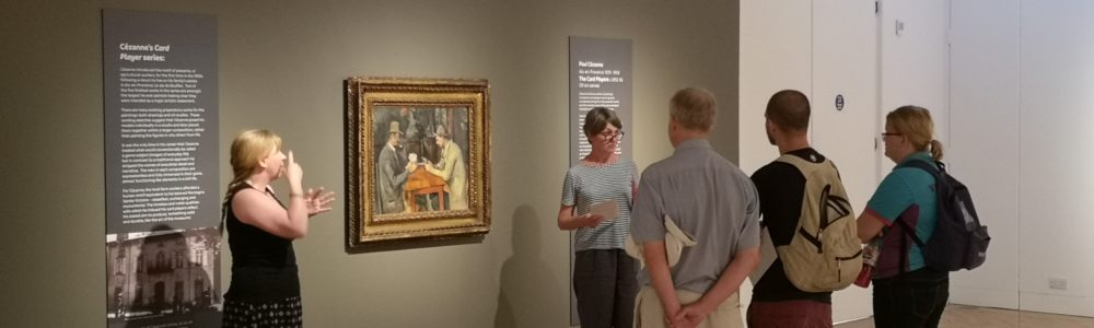 People watching a curator give a talk in front of Cezanne's Card Player painting